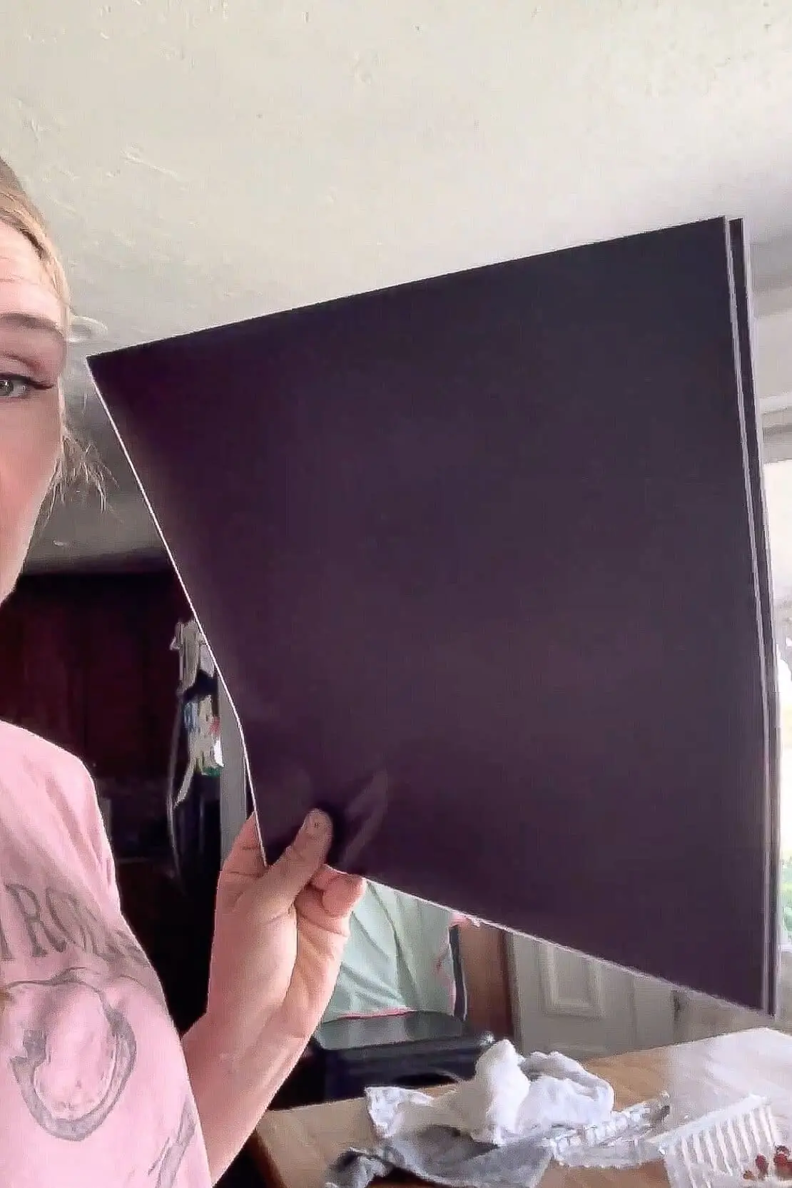 Woman holding a large sheet of black adhesive vinyl before cutting it down for a DIY black window grid makeover.